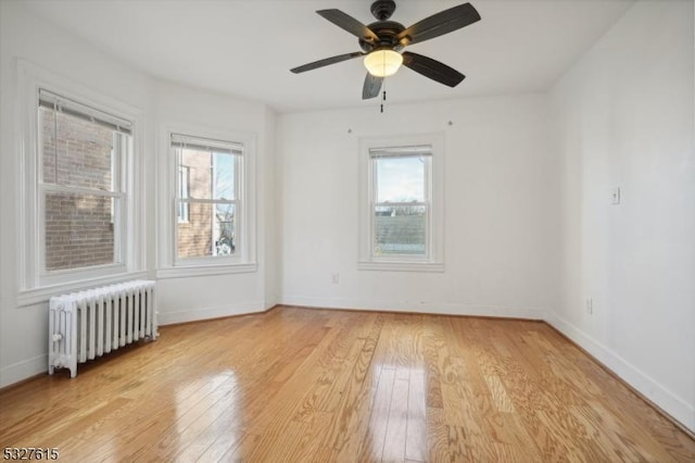 empty room featuring radiator, ceiling fan, and light wood-type flooring