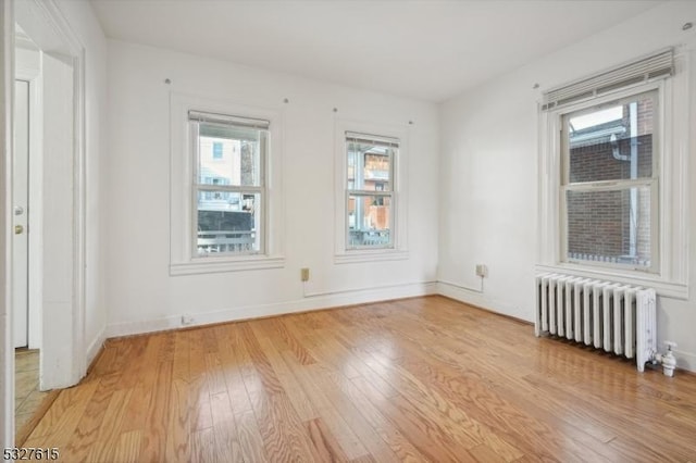 unfurnished room featuring radiator heating unit, a healthy amount of sunlight, and light wood-type flooring