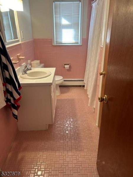 bathroom featuring vanity, a baseboard radiator, toilet, and tile walls