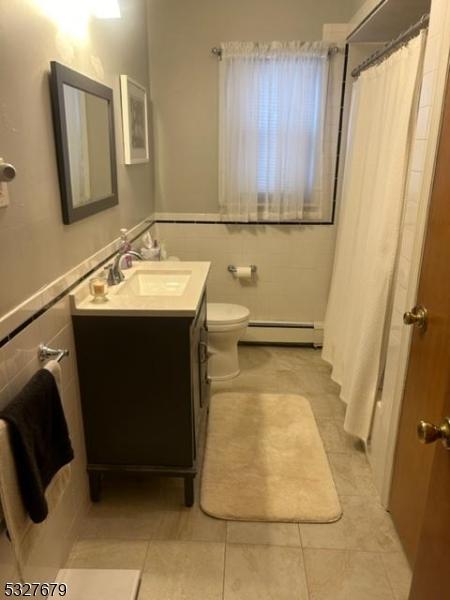 bathroom with vanity, tile patterned floors, toilet, baseboard heating, and tile walls