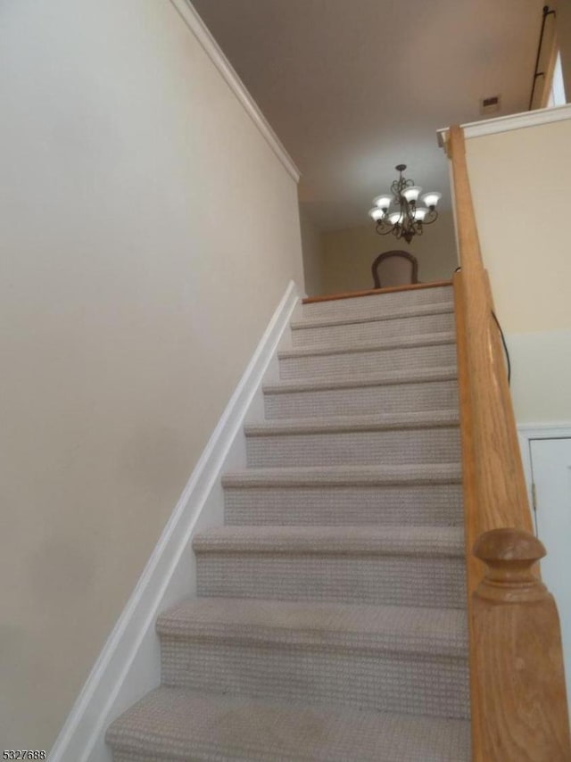 stairway featuring crown molding and an inviting chandelier