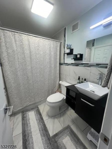 bathroom with vanity, toilet, and tile walls