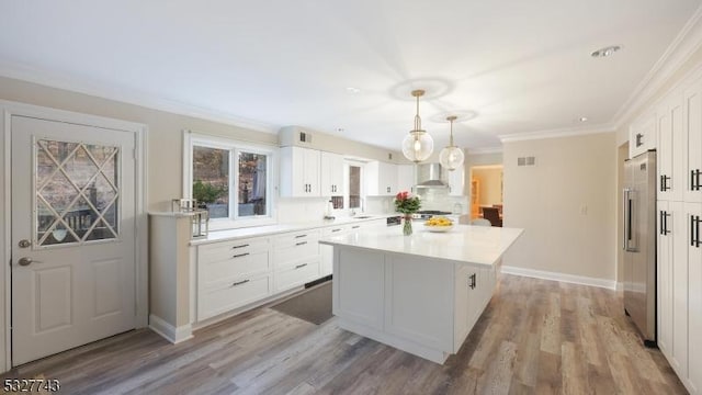 kitchen featuring wall chimney exhaust hood, pendant lighting, a center island, high quality fridge, and white cabinets