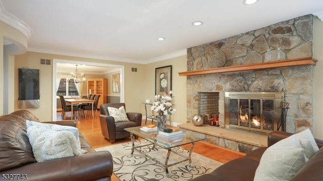 living room with light wood-type flooring, a stone fireplace, an inviting chandelier, and crown molding