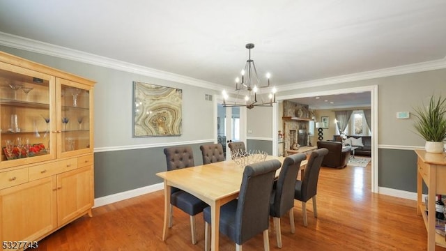 dining area with ornamental molding, light hardwood / wood-style floors, a notable chandelier, and a fireplace