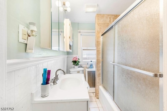 full bathroom featuring tile patterned floors, vanity, shower / bath combination with glass door, tile walls, and toilet