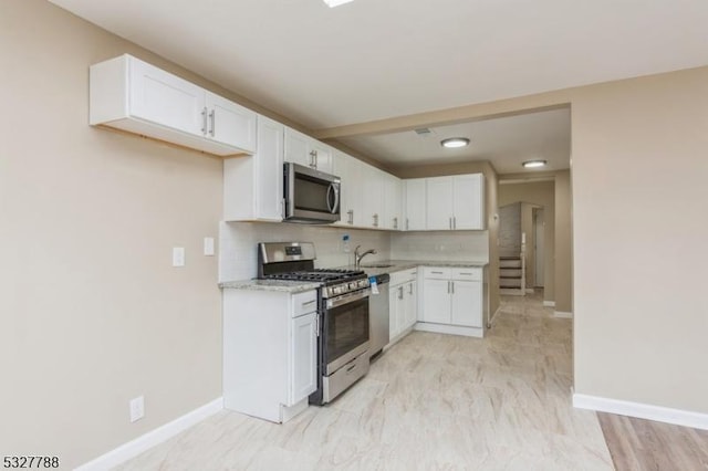 kitchen with decorative backsplash, light stone counters, stainless steel appliances, light hardwood / wood-style flooring, and white cabinets