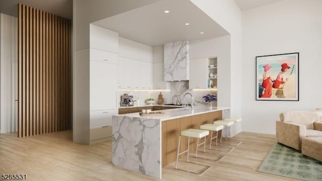 kitchen with white cabinetry, tasteful backsplash, light hardwood / wood-style flooring, kitchen peninsula, and a kitchen bar