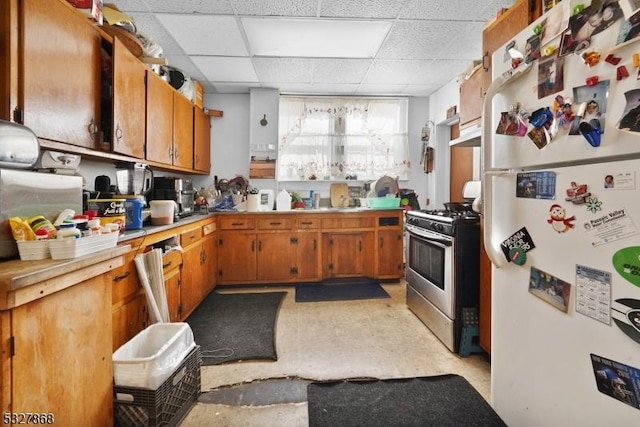 kitchen featuring stainless steel gas range oven, a drop ceiling, white refrigerator, and range hood