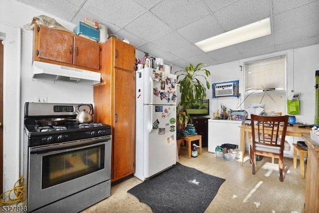 kitchen with white refrigerator, a wall unit AC, stainless steel gas range oven, and a paneled ceiling