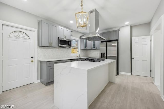 kitchen with hanging light fixtures, a kitchen island, light wood-type flooring, appliances with stainless steel finishes, and island range hood