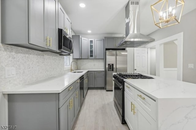 kitchen with appliances with stainless steel finishes, light wood-type flooring, exhaust hood, pendant lighting, and gray cabinets