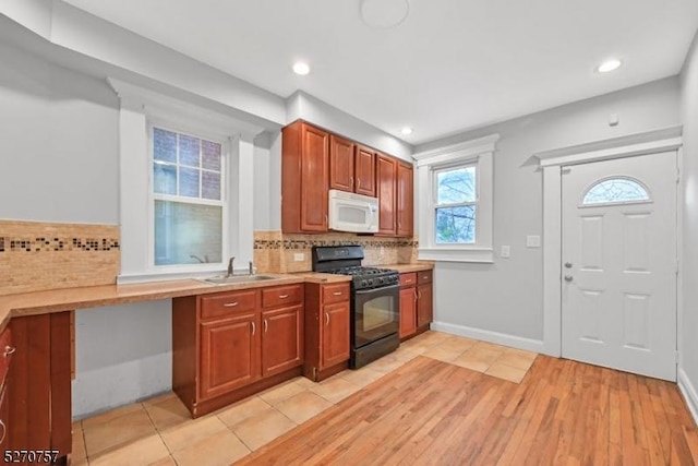 kitchen featuring decorative backsplash, black gas range oven, light hardwood / wood-style floors, and sink