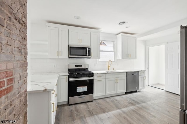 kitchen with sink, appliances with stainless steel finishes, light hardwood / wood-style floors, white cabinetry, and brick wall