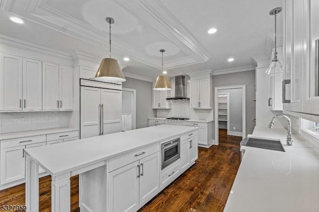 kitchen featuring dark hardwood / wood-style flooring, wall chimney exhaust hood, pendant lighting, built in appliances, and white cabinetry