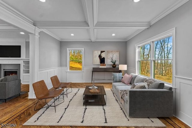 living room with wood-type flooring, plenty of natural light, ornamental molding, and beam ceiling