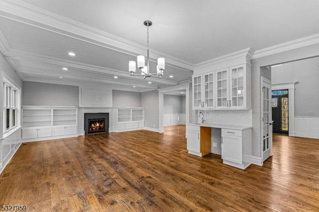 unfurnished living room with built in shelves, sink, dark hardwood / wood-style flooring, a notable chandelier, and ornamental molding