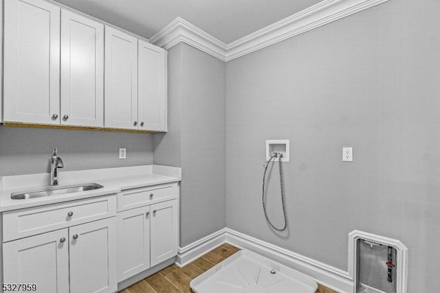 clothes washing area with cabinets, sink, hookup for a washing machine, ornamental molding, and wood-type flooring