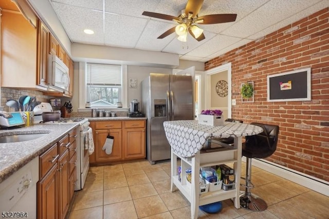 kitchen with a drop ceiling, sink, brick wall, white appliances, and light tile patterned floors