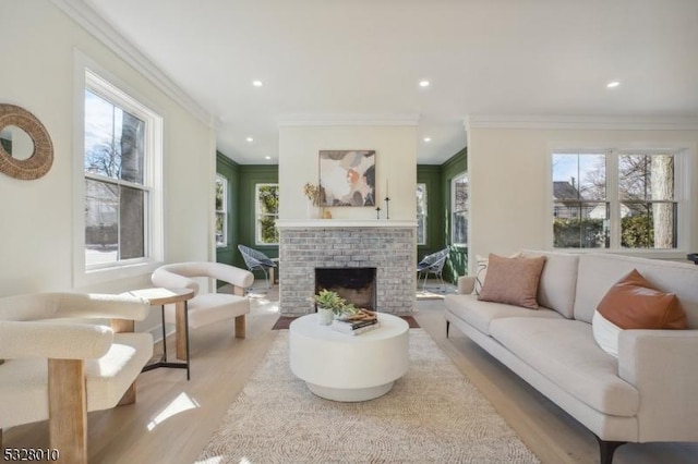 living area with ornamental molding, recessed lighting, a brick fireplace, and light wood-style flooring