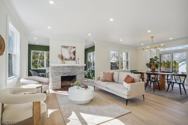 living room featuring a notable chandelier, recessed lighting, a fireplace, light wood-style floors, and crown molding