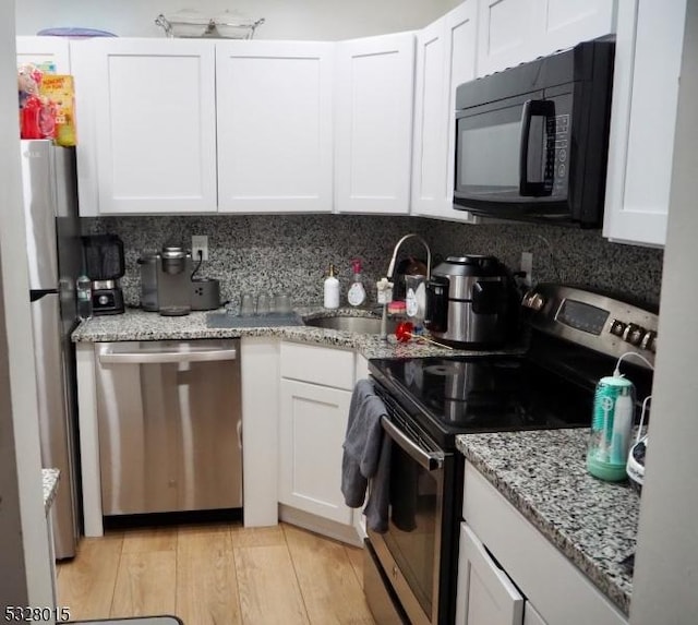 kitchen with white cabinetry, sink, light stone counters, light hardwood / wood-style flooring, and appliances with stainless steel finishes