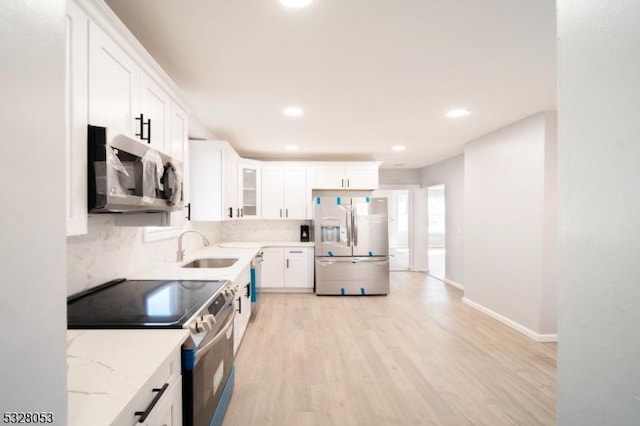 kitchen featuring sink, decorative backsplash, light wood-type flooring, appliances with stainless steel finishes, and white cabinetry