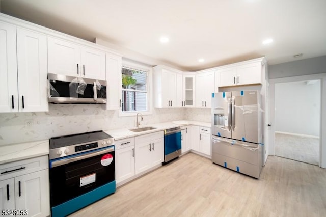 kitchen with light stone countertops, stainless steel appliances, sink, light hardwood / wood-style floors, and white cabinetry