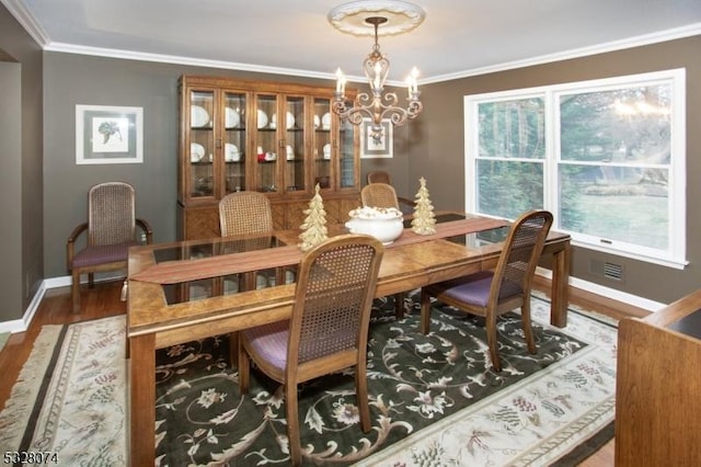 dining area with wood-type flooring, ornamental molding, and an inviting chandelier