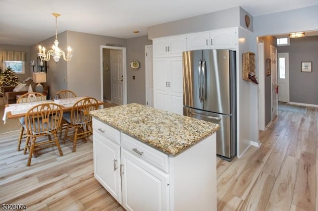 kitchen featuring a center island, an inviting chandelier, hanging light fixtures, white cabinetry, and stainless steel refrigerator