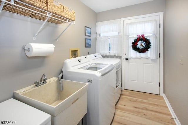 laundry area featuring washing machine and dryer, sink, and light hardwood / wood-style floors