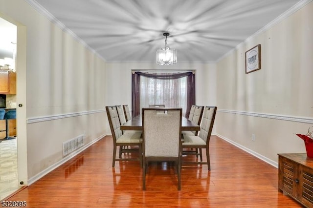 dining room with ornamental molding, a notable chandelier, and light hardwood / wood-style flooring