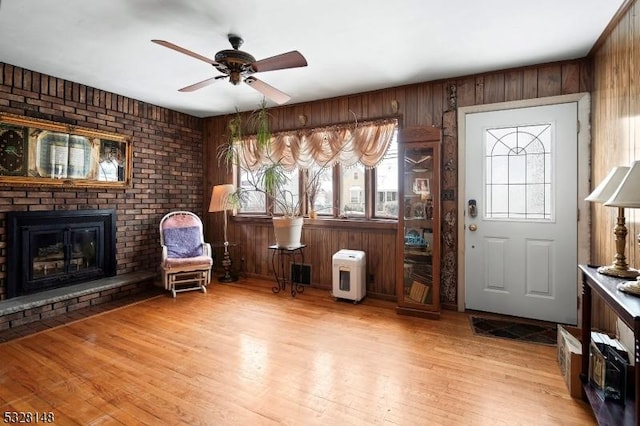 entrance foyer with ceiling fan, wood walls, light hardwood / wood-style flooring, and a brick fireplace