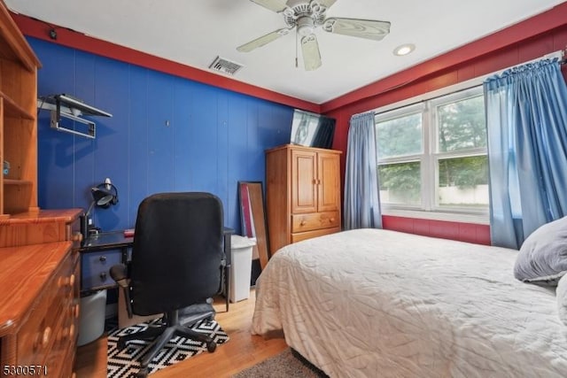 bedroom featuring light hardwood / wood-style floors, ceiling fan, and wooden walls