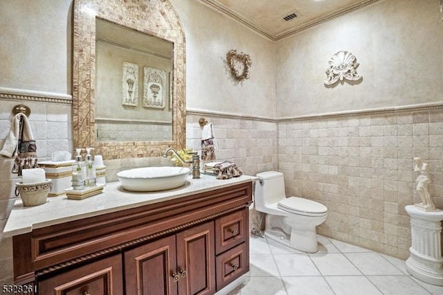 bathroom featuring tile patterned floors, crown molding, toilet, vanity, and tile walls