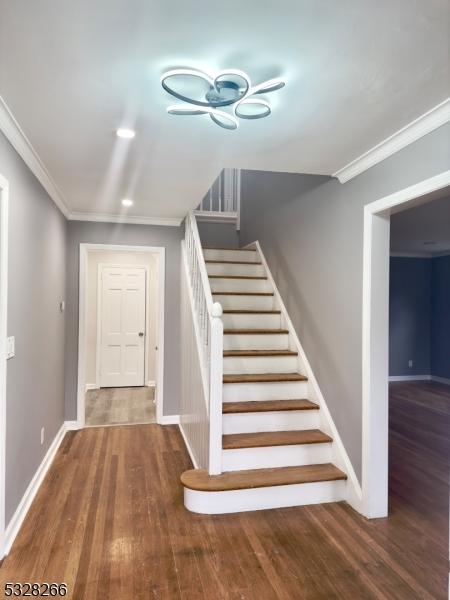 stairs with wood-type flooring and crown molding