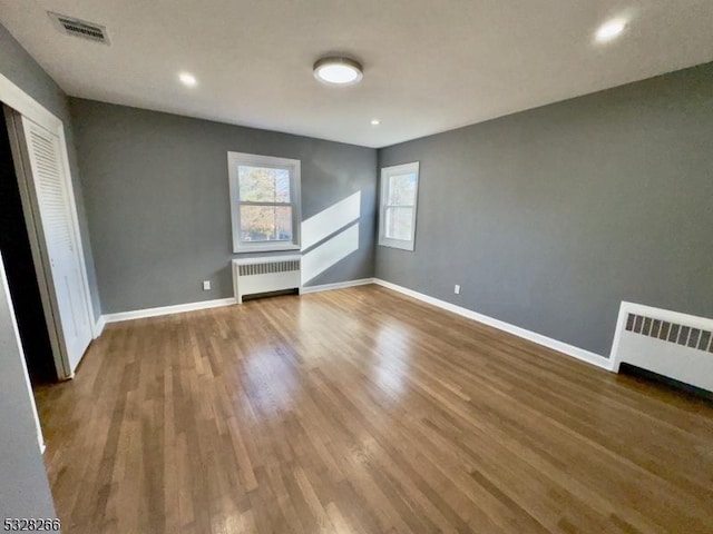 unfurnished bedroom featuring wood-type flooring, radiator, and a closet