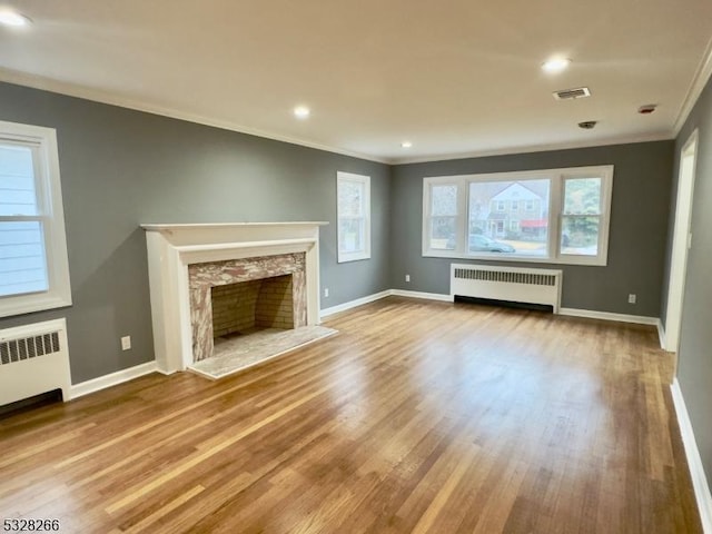 unfurnished living room featuring radiator heating unit, a premium fireplace, ornamental molding, and wood-type flooring