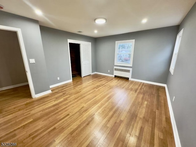 unfurnished bedroom with radiator, a spacious closet, and light hardwood / wood-style floors