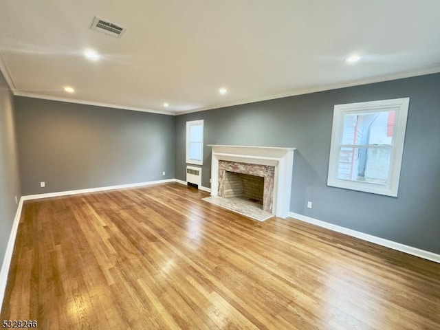 unfurnished living room featuring light hardwood / wood-style floors, a stone fireplace, radiator, and crown molding