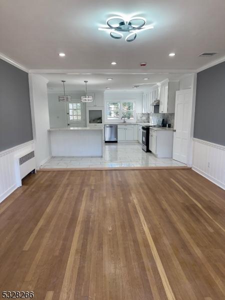 unfurnished living room with light hardwood / wood-style floors, radiator heating unit, and ornamental molding