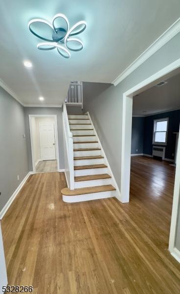 stairway with wood-type flooring, radiator heating unit, and crown molding