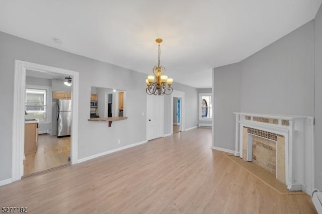 unfurnished living room with ceiling fan with notable chandelier, light hardwood / wood-style floors, baseboard heating, and a tiled fireplace