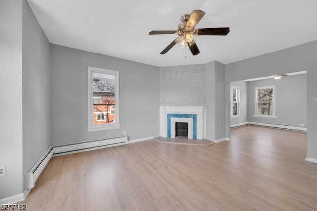 unfurnished living room with ceiling fan, a baseboard heating unit, a tiled fireplace, and light hardwood / wood-style flooring