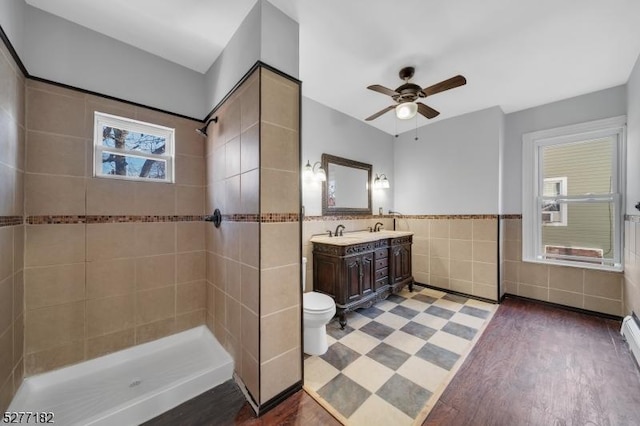 bathroom featuring a tile shower, wood-type flooring, toilet, vanity, and tile walls