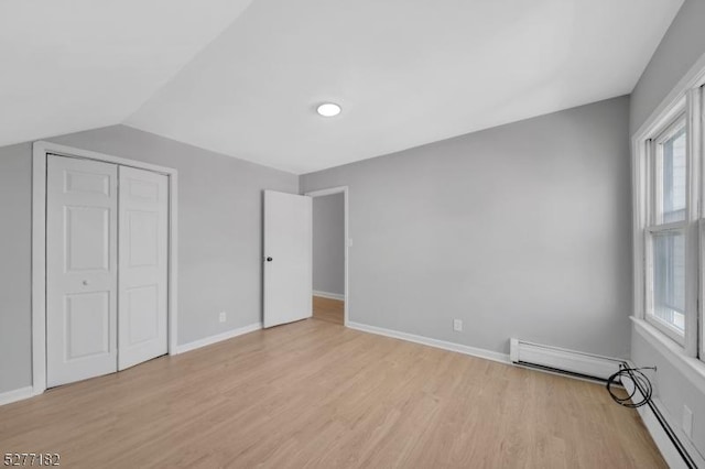 unfurnished bedroom featuring light wood-type flooring, a closet, baseboard heating, and multiple windows