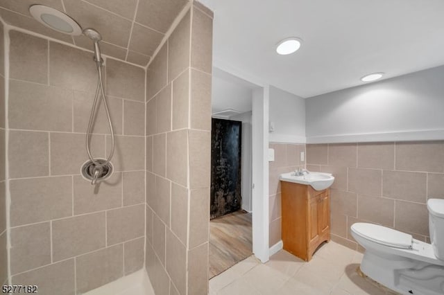 bathroom featuring a tile shower, vanity, tile walls, tile patterned flooring, and toilet