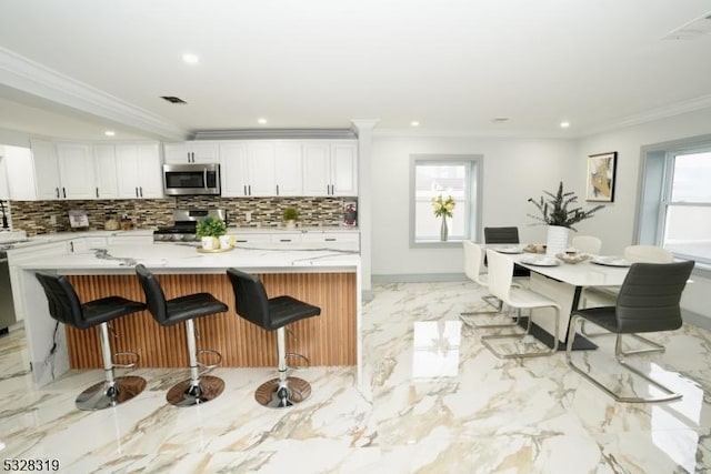 kitchen featuring a kitchen bar, appliances with stainless steel finishes, ornamental molding, a kitchen island, and white cabinetry