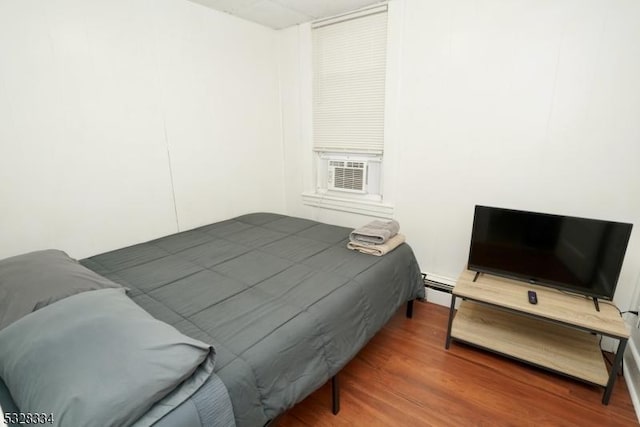 bedroom with cooling unit, a baseboard radiator, and hardwood / wood-style flooring