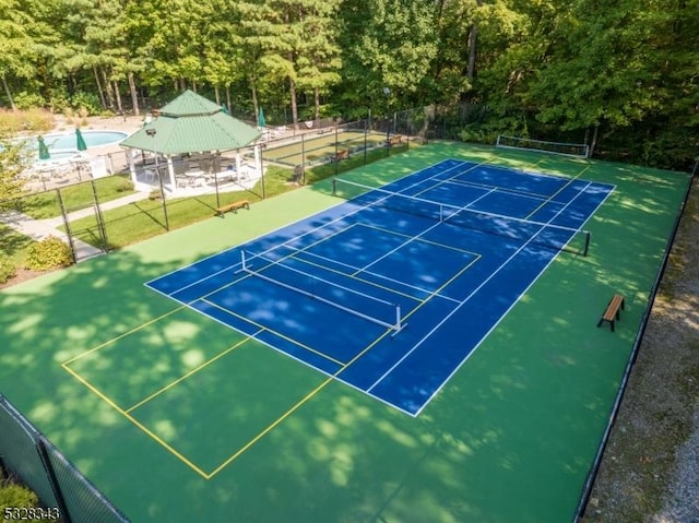view of tennis court with a forest view, a gazebo, and fence
